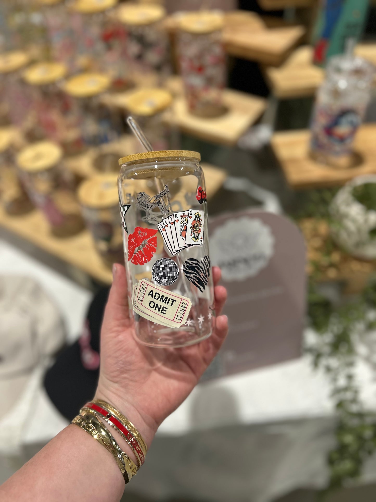Clear tumbler with poker-themed design held by a hand, with blurred background of similar tumblers.