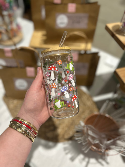 Hand holding a transparent tumbler with forest-themed design in front of blurred boxes.