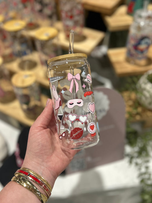 Clear glass tumbler with Sabrina Carpenter decorative stickers held by a hand in a store setting.