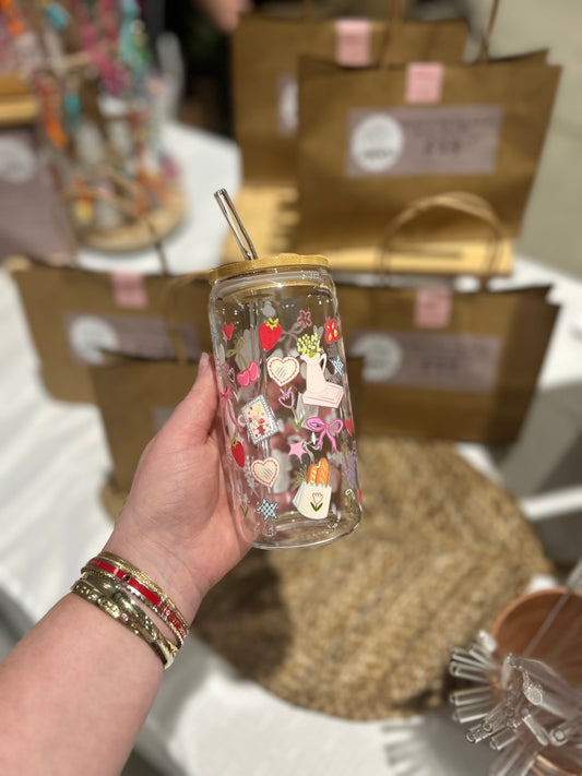Hand holding a clear tumbler with colorful cute designs against a blurred background of gift boxes.