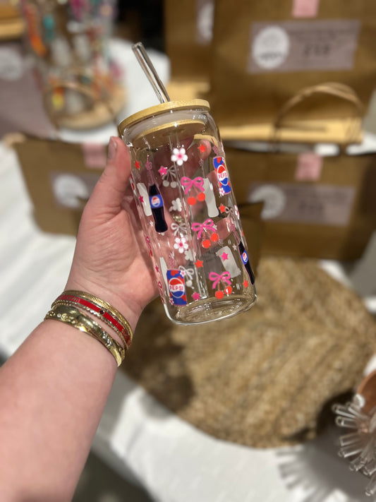 Hand holding a transparent tumbler with colorful designs, including Pepsi logos, against a blurred background.