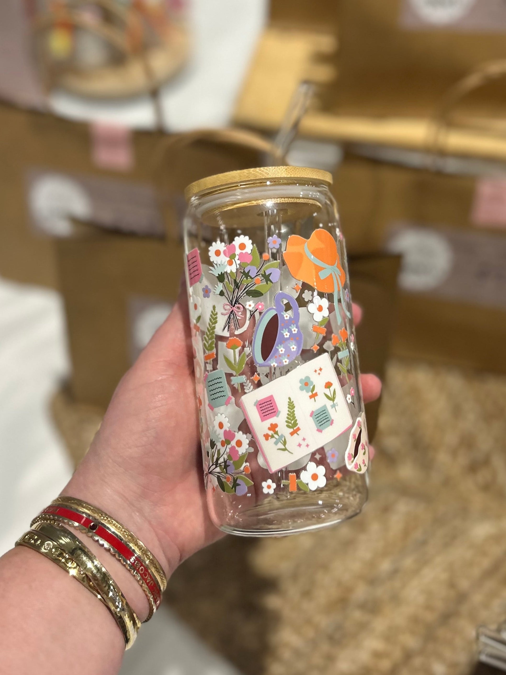 Hand holding a decorated glass jar with floral patterns, surrounded by brown paper bags.