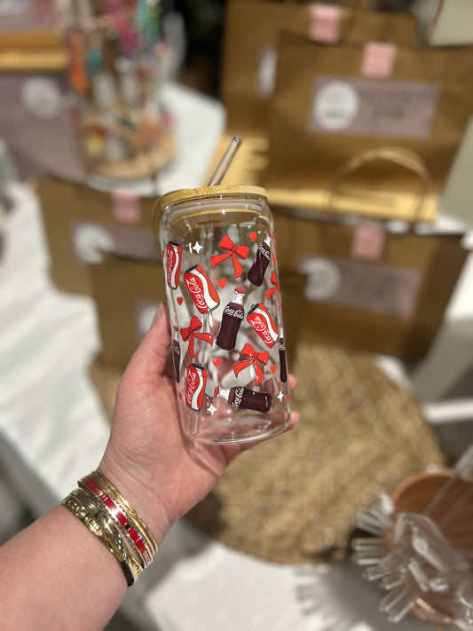 Hand holding a clear tumbler with Coca-Cola-themed design against a blurred indoor background
