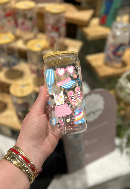 Hand holding a Clear glass cup with colorful  pickleball  design against a blurred store background