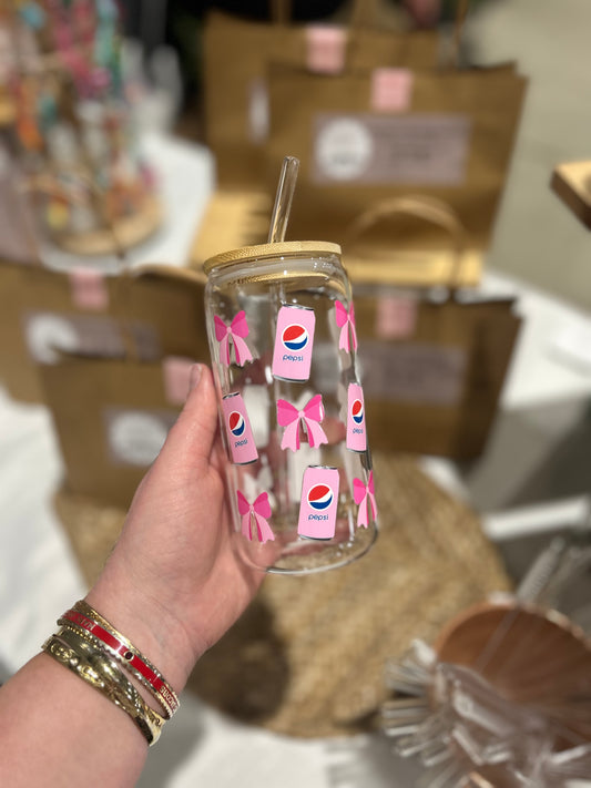 Hand holding a glass tumbler with Pepsi logo and pink designs, blurred background
