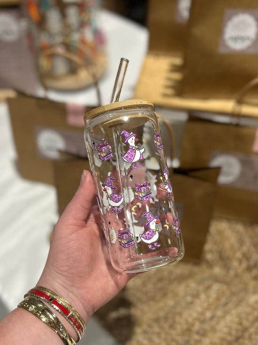 Hand holding a clear mug with purple witch ducks against a blurred store background