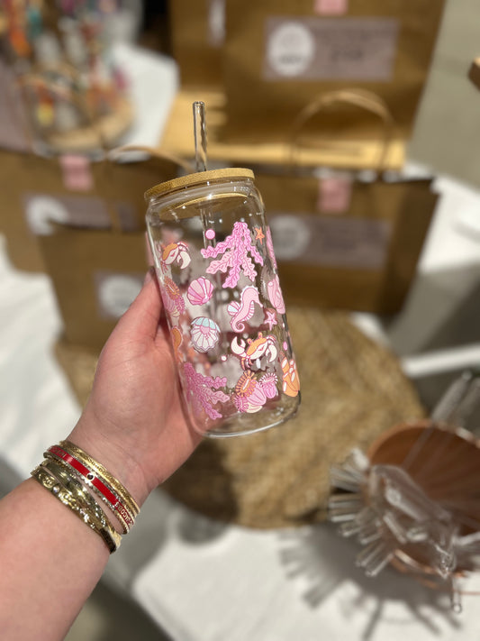 Hand holding a glass tumbler with pink under the sea design and bamboo lid, blurred background